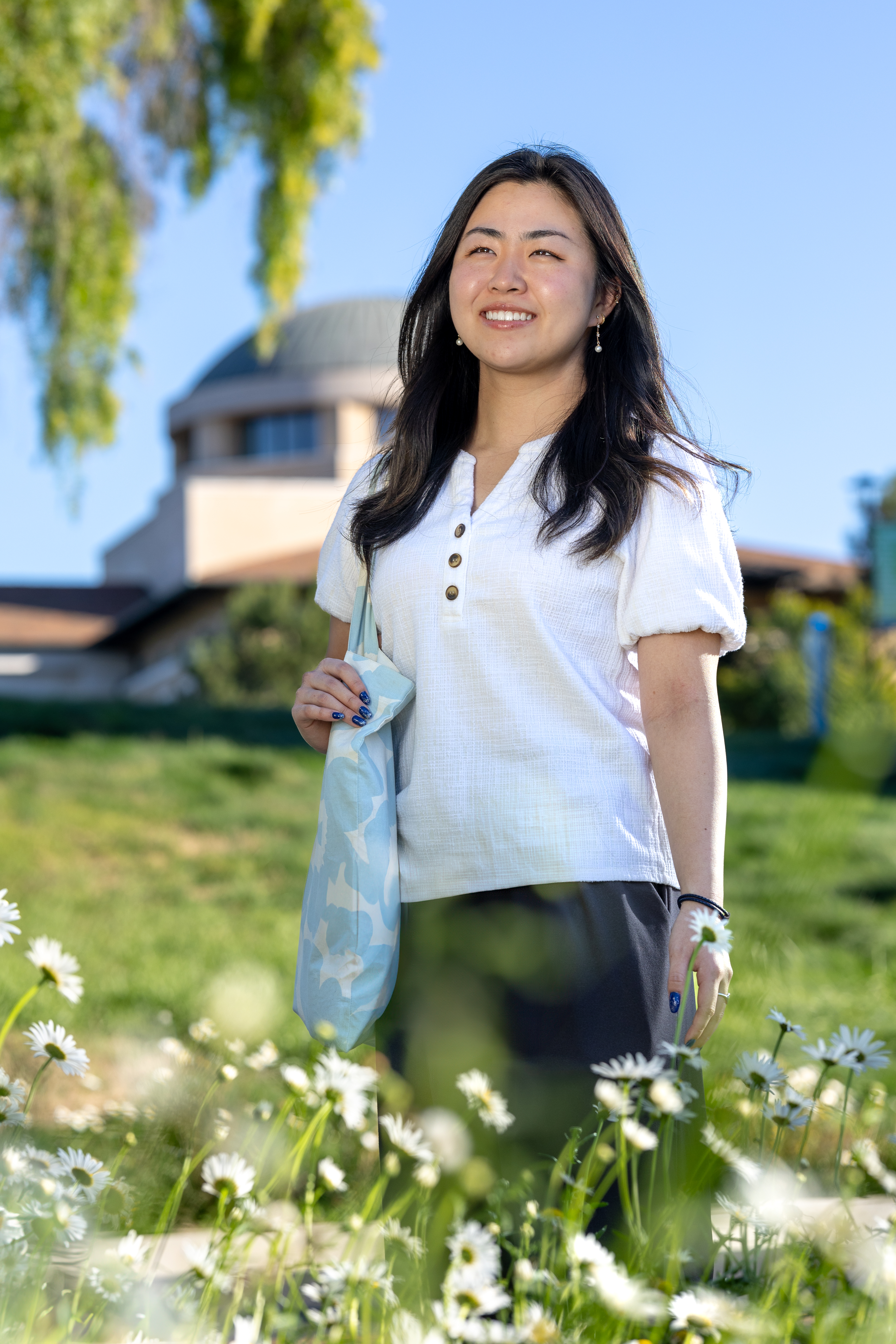 Liona Shoji smiles in front of Founders Hall surrounded by white flowers.