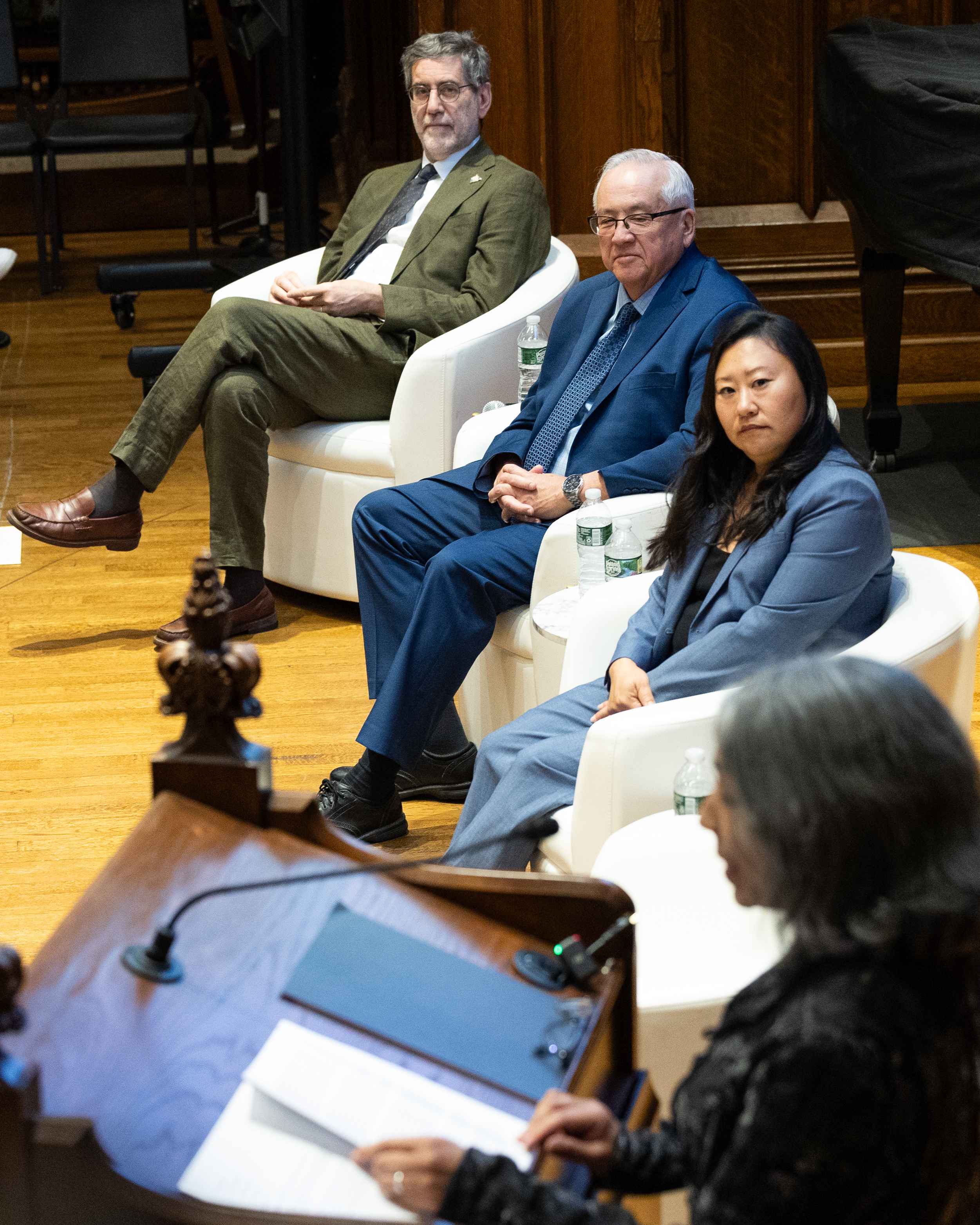 Vertical shot of the three panelists looking on and listening to a speaker standing at a wooden lectern.