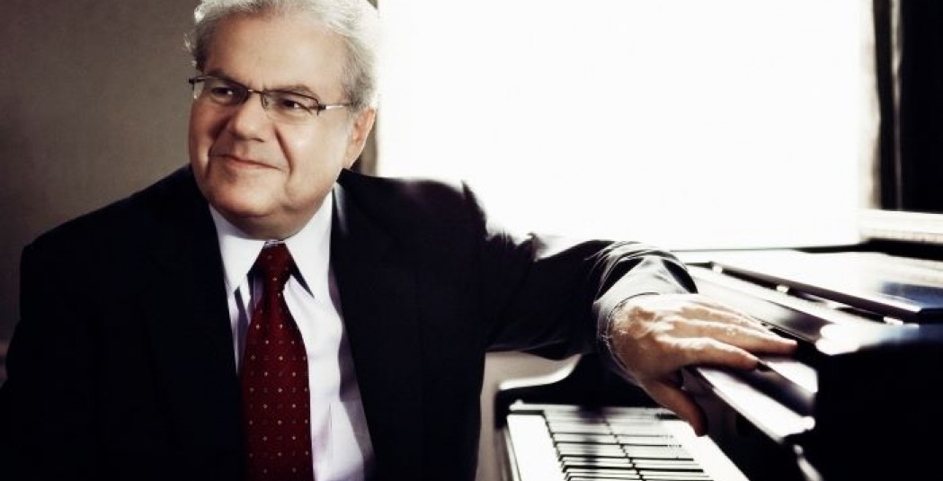 Emanuel Ax sitting at a piano wearing a suit
