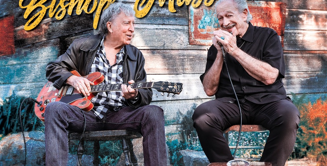 Two men sitting on chairs playing the guitar and a harmonica