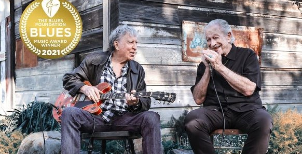 Elvin Bishop & Charlie Musselwhite sitting and playing harmonica and guitar