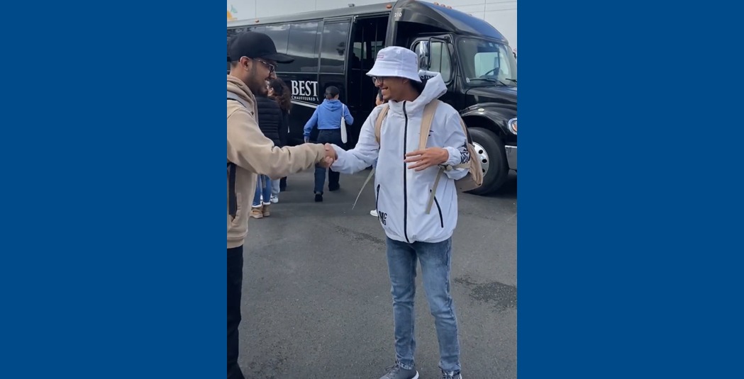 Two students wearing hats shake hands