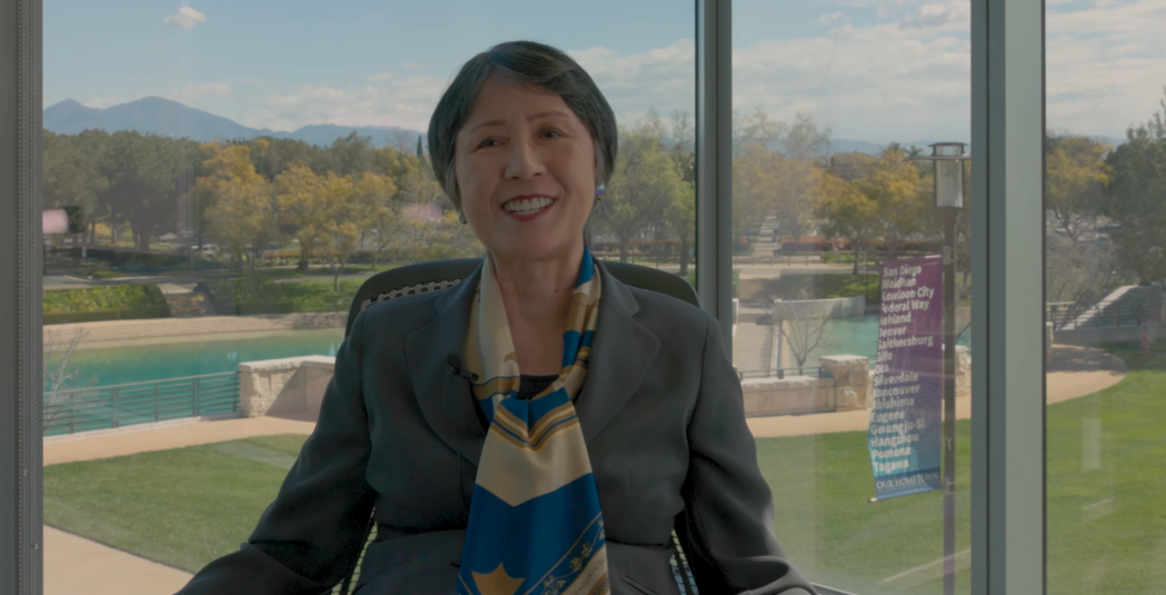Tomoko Takahashi smiles in a meeting room with glass windows overlooking Peace Lake and Founders walk.