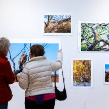 Two women wearing winter jackets point at photographs in the exhibition.