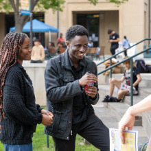 Two students wearing all black laugh while chatting with others on the Campus Green during SUA's Homecoming celebration.