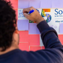 The back of a brown-haired person's head is out of focus as they sign a commemorative message on light purple paper.