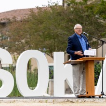 SUA President Ed Feasel addresses the crowd at the 2025 Homecoming event while standing in front of large block letters spelling "SOKA"