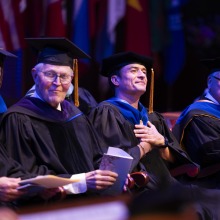 Stephen Dunham, Orlando Bloom, Ed Feasel, and other faculty members wear their cap and gowns and listen during commencement.
