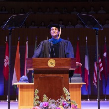 Orlando Bloom stands at the lectern and delivers his keynote during commencement.