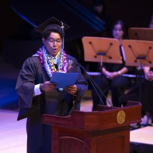A graduating student looks intently at his speech as he delivers it to the crowd at commencement.