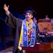 Jordan Bravo '25 gestures to the crowd during his speech at SUA's 2025 commencement ceremony.