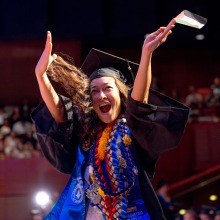 An excited graduate holds up her diploma in celebration.