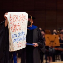 A graduate holds up a sign saying "thank you" in multiple languages