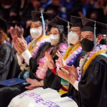 A row of masked graduates applaud