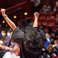 A graduate raises both arms in celebration