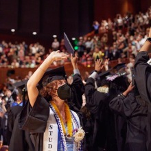 A masked graduate waves to the crowd