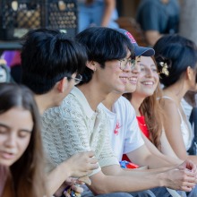 A group of students sit along the Campus Green and smile as they watch the activities unfold.