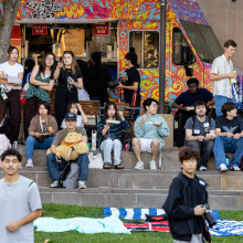 A large gathering of students sit on the steps and stand at the food truck during welcome back festivities.