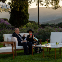 An older couple sitting on white outdoor lounge chairs 