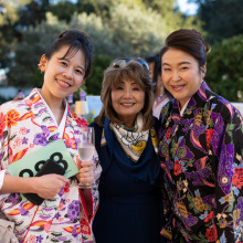 Three smiling women standing together at an outdoor reception