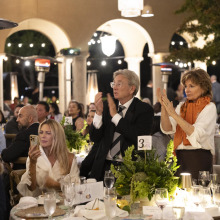 A man and a woman stand and clap at a dinner table