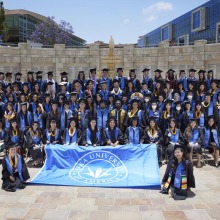 The Class of 2022 graduates pose in front of the Peace Lake Travertine Wall holding the Soka University of America banner