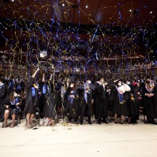 Graduates celebrate with gold and blue streamers flying around them