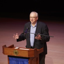 President Ed Feasel smiles as he stands at the podium and addresses the Class of 2026.