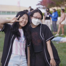 Two women pose for the camera, one is holding a peace sign, and the other is masked