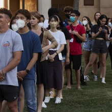 A group of students are standing in a vertical line, some are masked, others are smiling