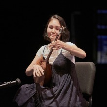A female student smiles as she plays a string instrument on stage