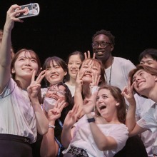 A group of students smile and hold up peace signs to the camera as they pose for a selfie.