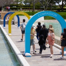 People walk through archways titled Wisdom, Courage, and Compassion across the walkways through Peace Lake.