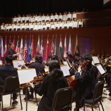 The band, band director, and chorus are seen with international flags in the background