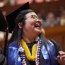 A happy graduate smiles to loved ones in the distance