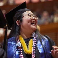 A happy graduate smiles to loved ones in the distance