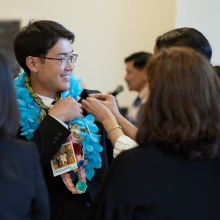A graduate has a lei placed on him by a friend