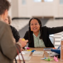 A woman at an information table gestures with her hands to a conference attendee.