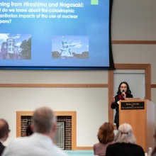 A female speaker gestures with her hand as she speaks into a microphone during the conference.