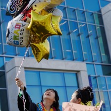 A graduate smiles looking up at the graduation balloons she's holding after commencement
