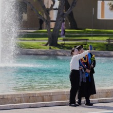 A graduate and their friend take a selfie in front of Peace Lake following commencement