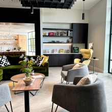 Interior shot of new Global Language and Culture Center featuring gray and green chairs, a velvet green couch, a bookcase with magazines, and a kitchen