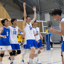 A group of volleyball players in white and blue "SOKA" jerseys celebrate a point on the court with cheers and raised arms.