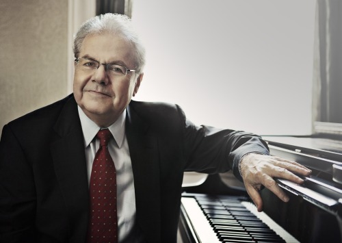 Man dressed in black sitting at piano facing camera