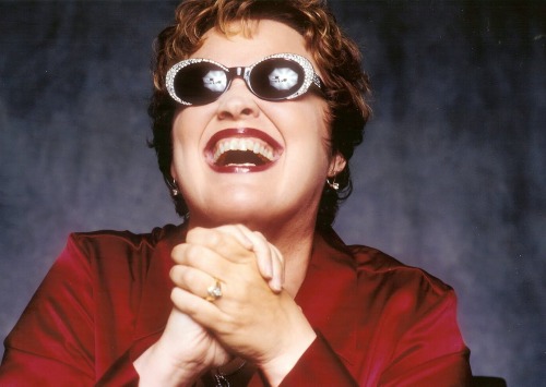 Woman in red suit with hands clasped laughing