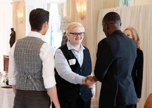 People dressed in business attire shake hands at an etiquette training event.