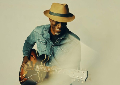 Man with hat in a blue shirt playing a guitar
