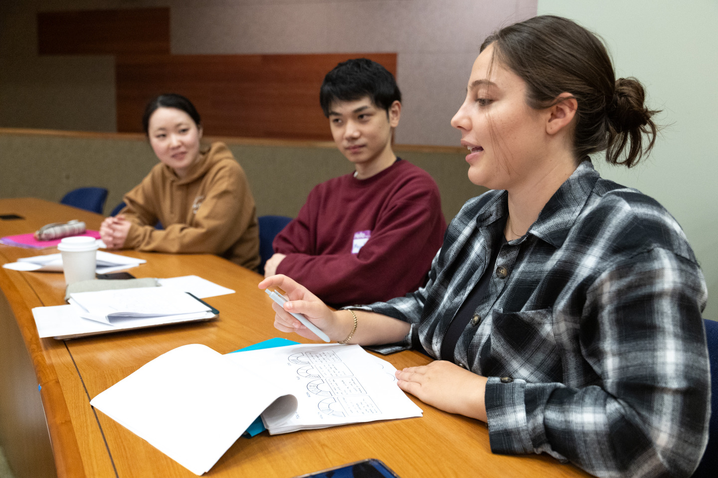 Three students work on packets of material on wooden desks during class.