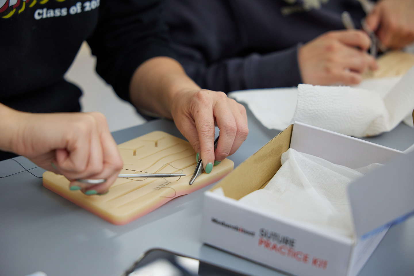 Two hands holding scissors pull a thread as students practice their sutures using a suture practice kit.