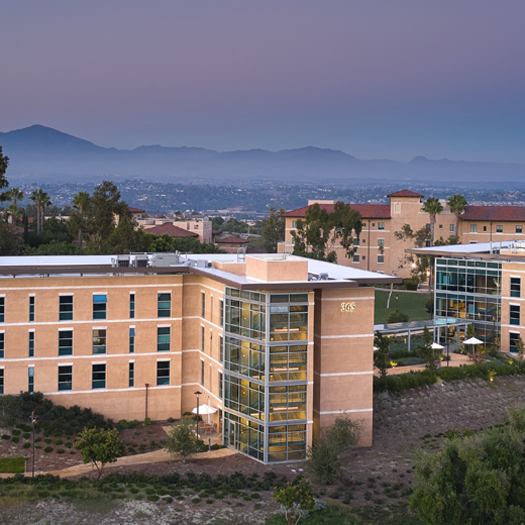 Aerial view of exterior of multiple residence halls on SUA's campus during sunset. The sky is purple and blue and there is a haze midway through the mountain range behind the residence halls.